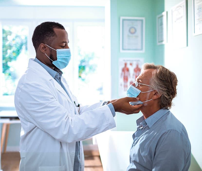 A Black doctor examining an elderly white male. Both are wearing mask