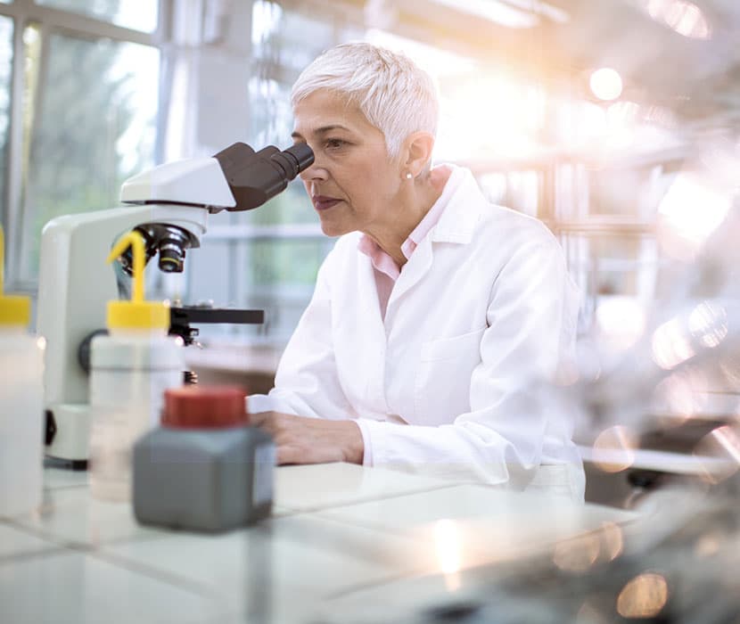 A generation x female lab tech looking in a microscope