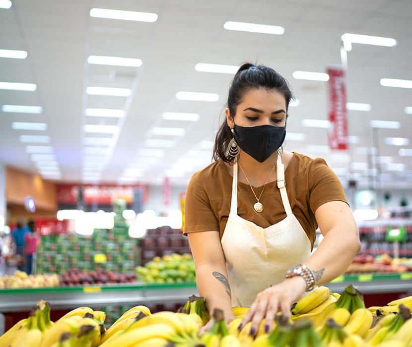 A grocery store clerk wearing a black mask stocking bananas.