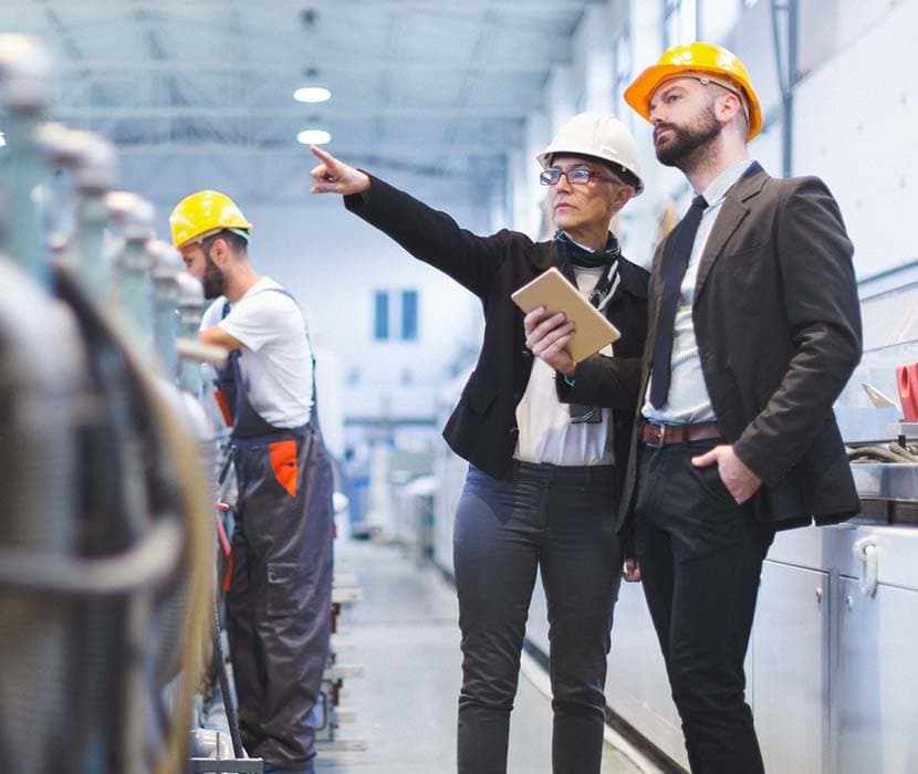 A female manager inside an industrial complex is wearing a white hard hat and pointing out in the distance.