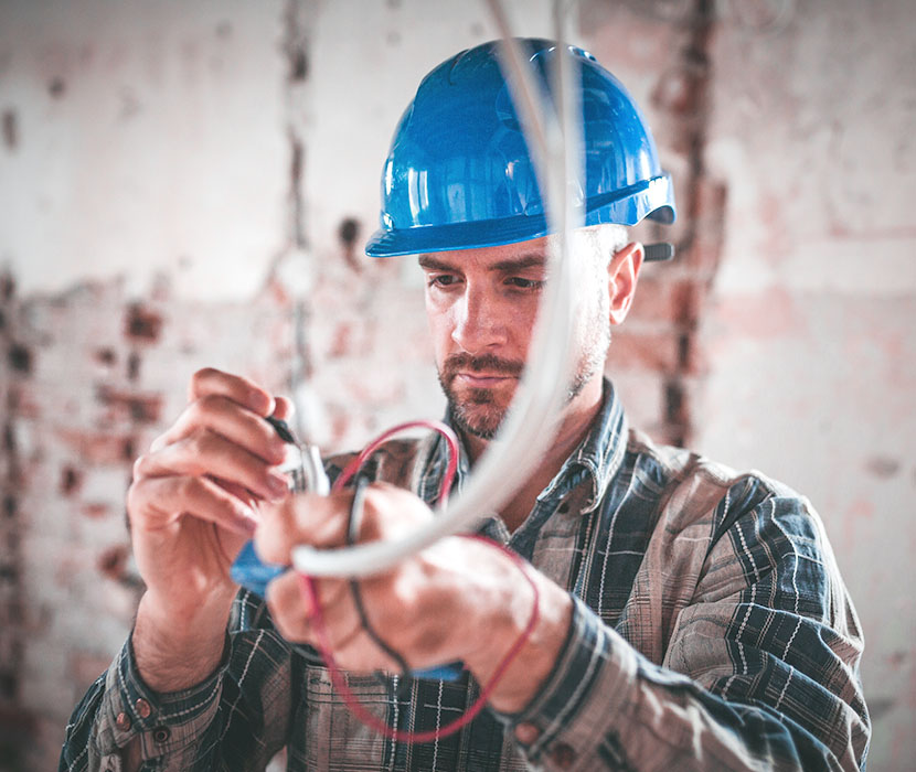 “A male with a hardhat on is working on electric wires.